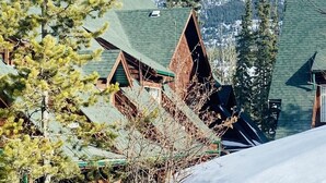 Una cabaña de montaña con un techo empinado, rodeada de árboles cubiertos de nieve y una montaña al fondo.