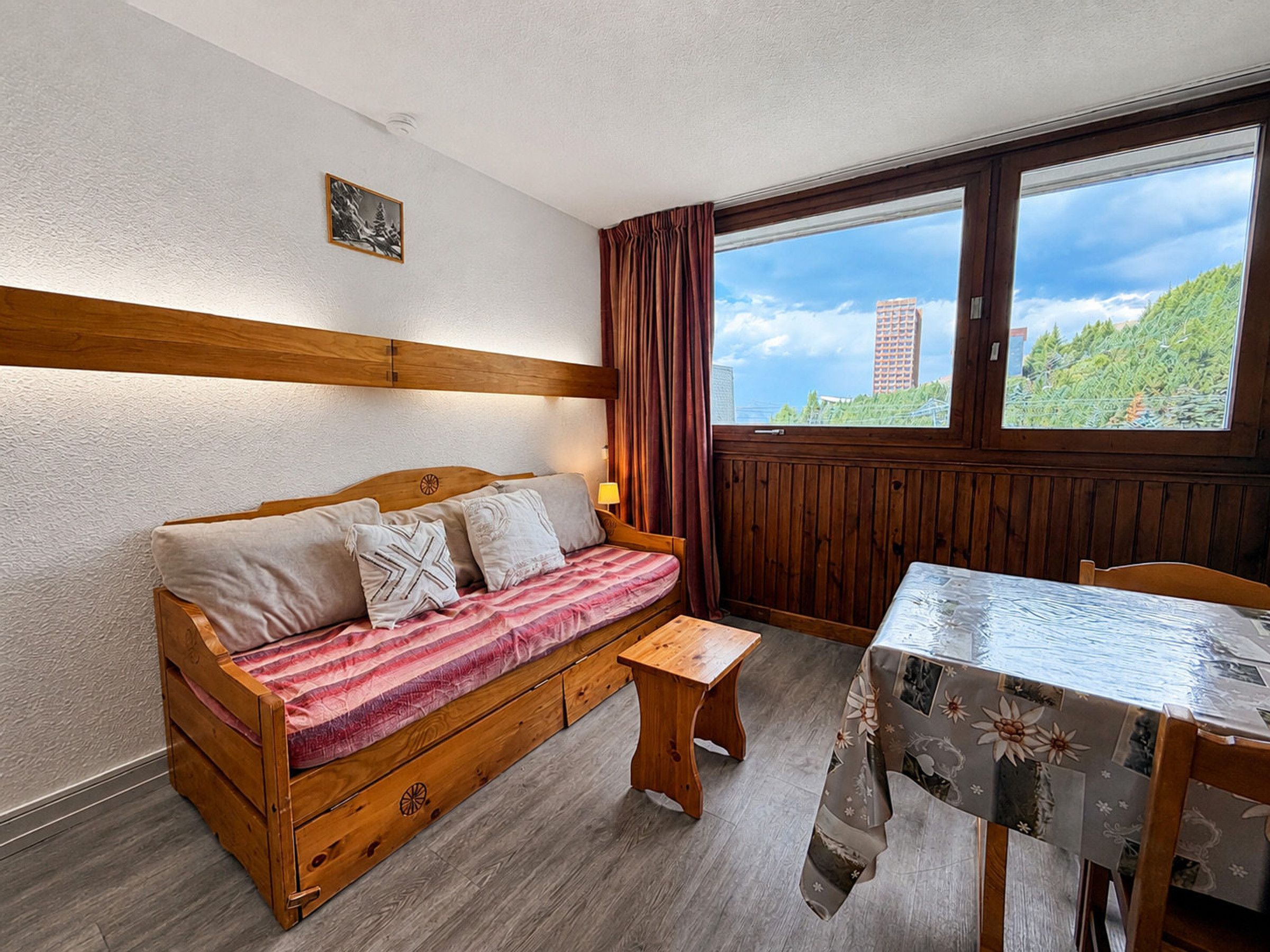 A cozy room with a wooden sofa, a small table, and a window with a view of a building and trees.