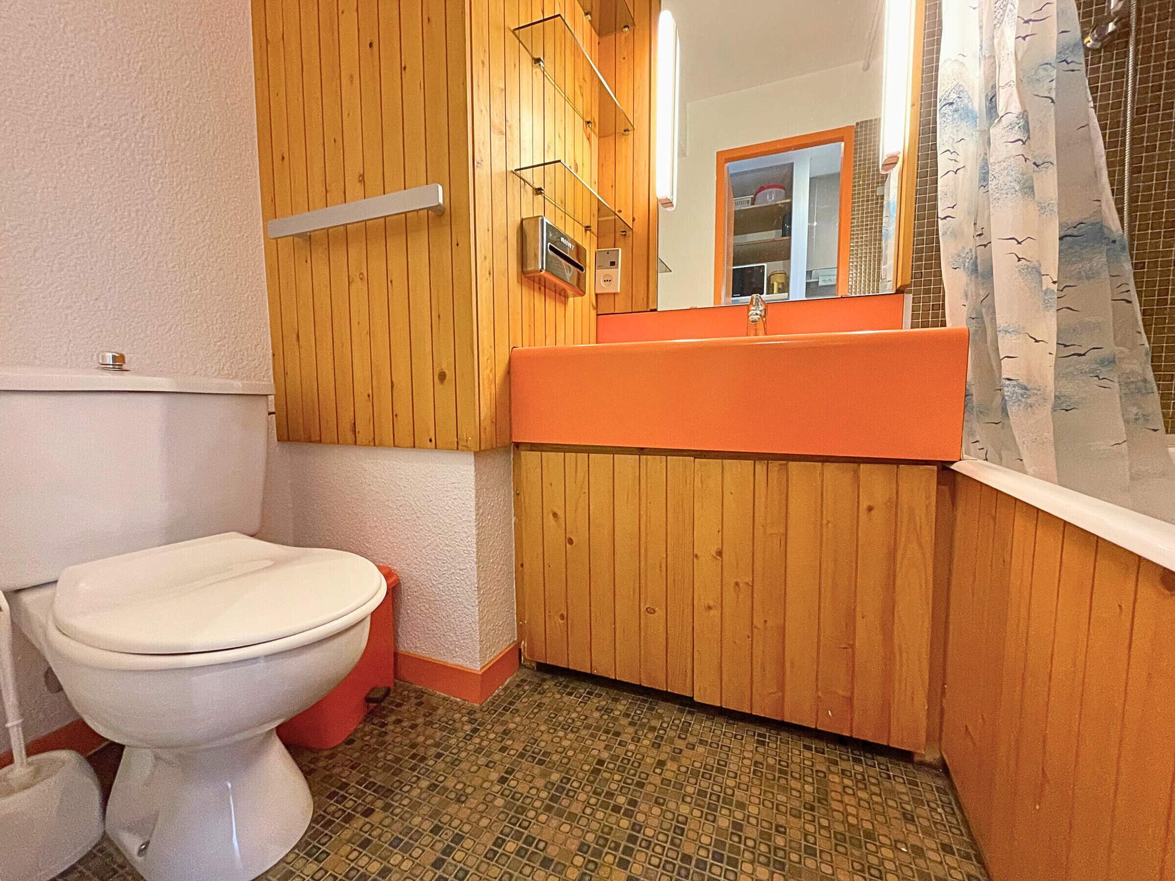A bathroom with a wooden vanity, a white toilet, and a tiled floor.