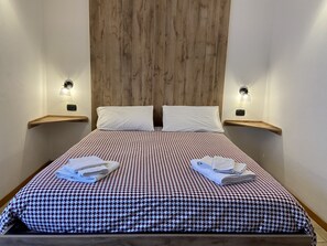 A neatly made bed with a checkered bedspread, two white pillows, and two towels folded on the bed. - 4Flats Orto di Venanzio (Barrea)