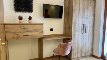 A modern room with a wooden desk, a pink chair, a TV, and a wardrobe.