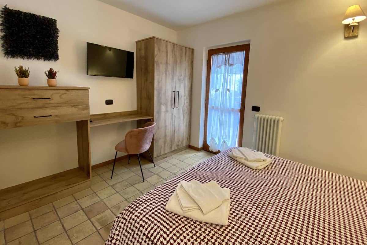 Une chambre à coucher avec un lit, un bureau, une chaise, un téléviseur et une fenêtre avec des rideaux.