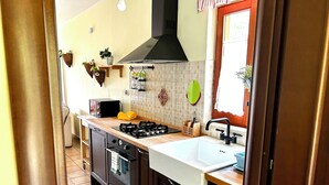 A kitchen with a stove, sink, and oven. There are hanging baskets and a window with curtains. - 4Flats Orto di Venanzio (Barrea)