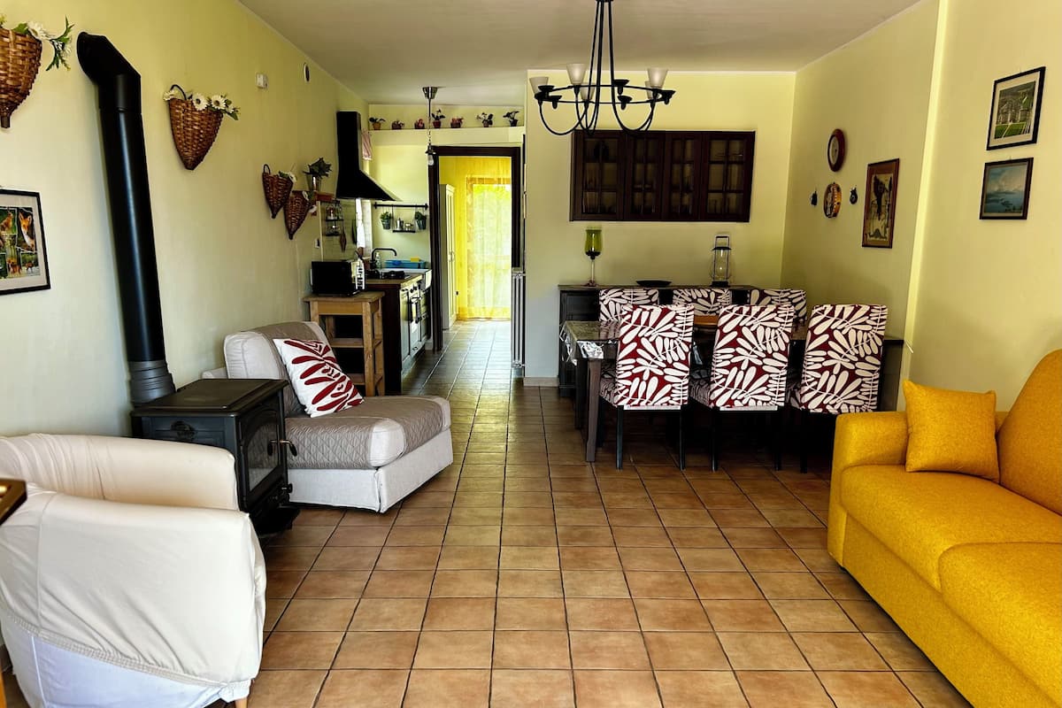 Un salon avec un canapé, une table à manger entourée de chaises, une cheminée et, au fond, un coin cuisine.