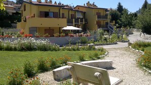 A yellow building with multiple balconies and a garden with flowers and a bench. - 4Flats Orto di Venanzio (Barrea)