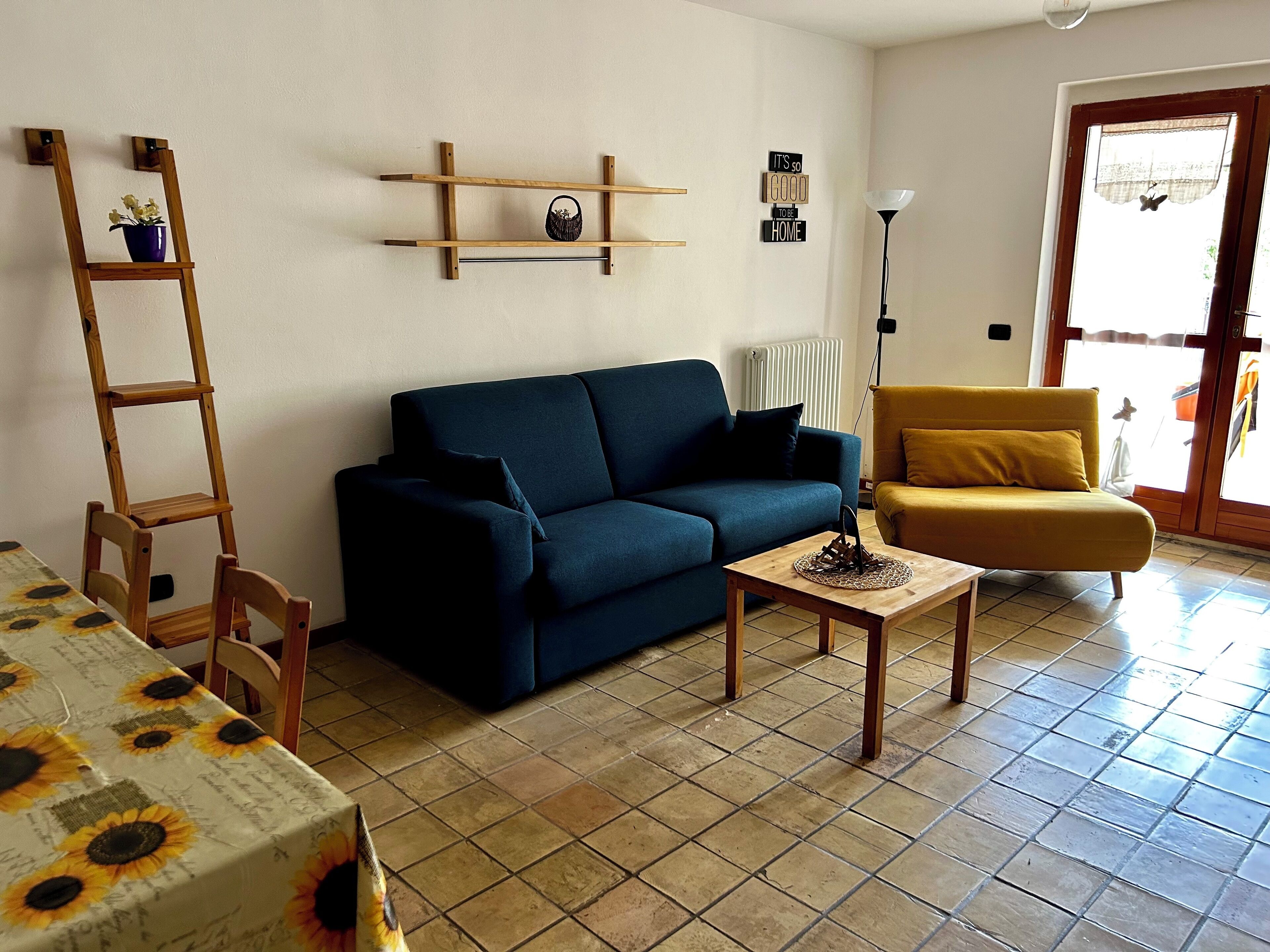 A living room with a blue sofa, a yellow armchair, a wooden coffee table, and a wooden ladder against the wall.