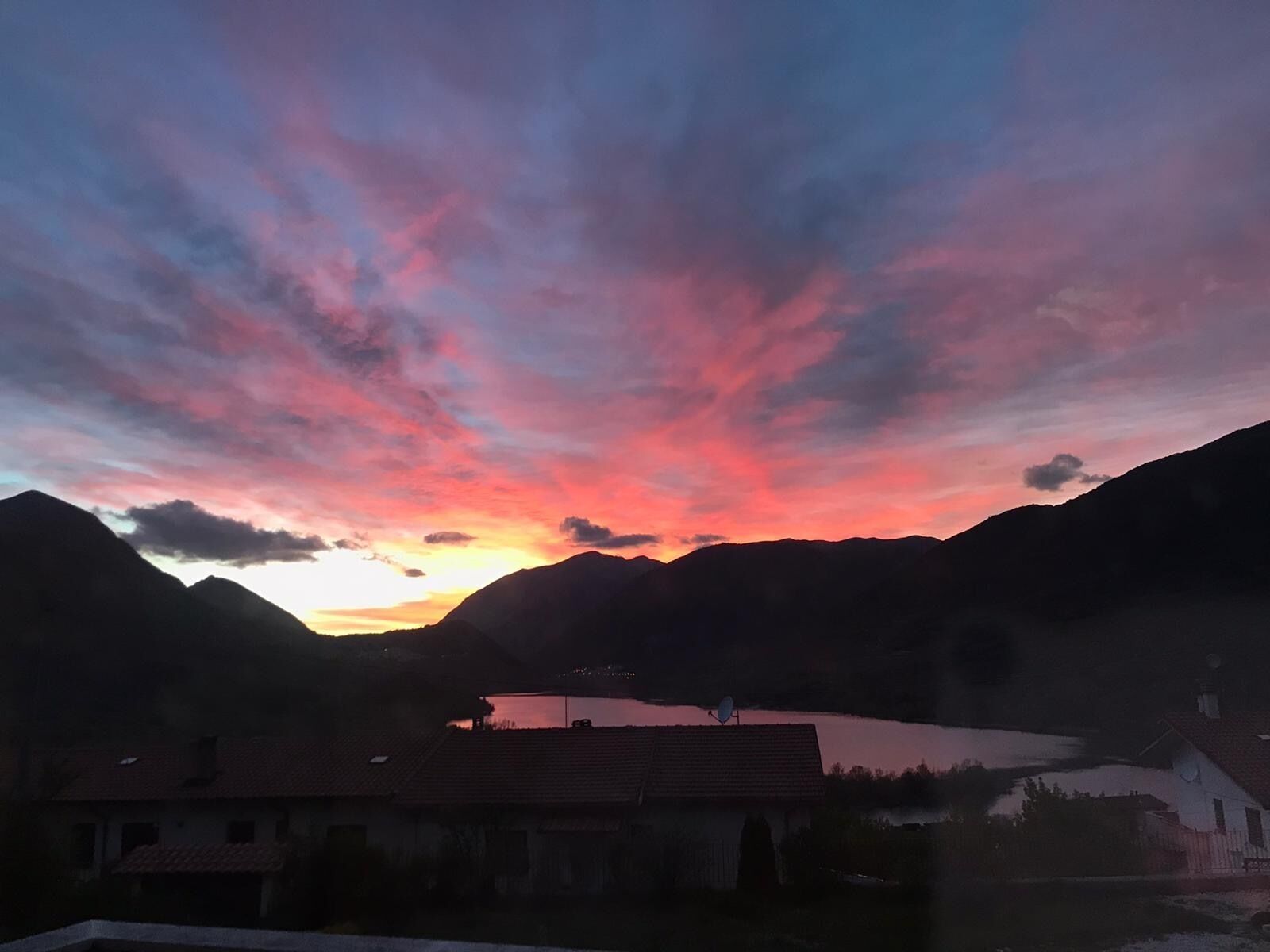 Ett bergigt landskap med en solnedgång över en sjö, omgivet av hus.