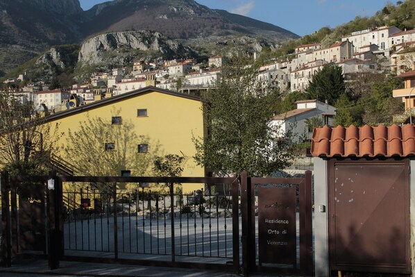 A yellow building with a gated entrance, surrounded by a mountainous landscape and residential buildings. - 4Flats Orto di Venanzio (Barrea)