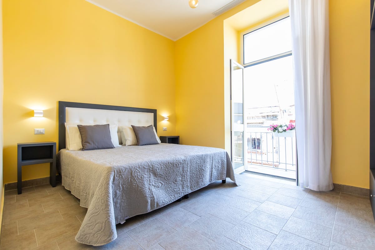 A bedroom with a bed, nightstands, a window, and a balcony with flowers.