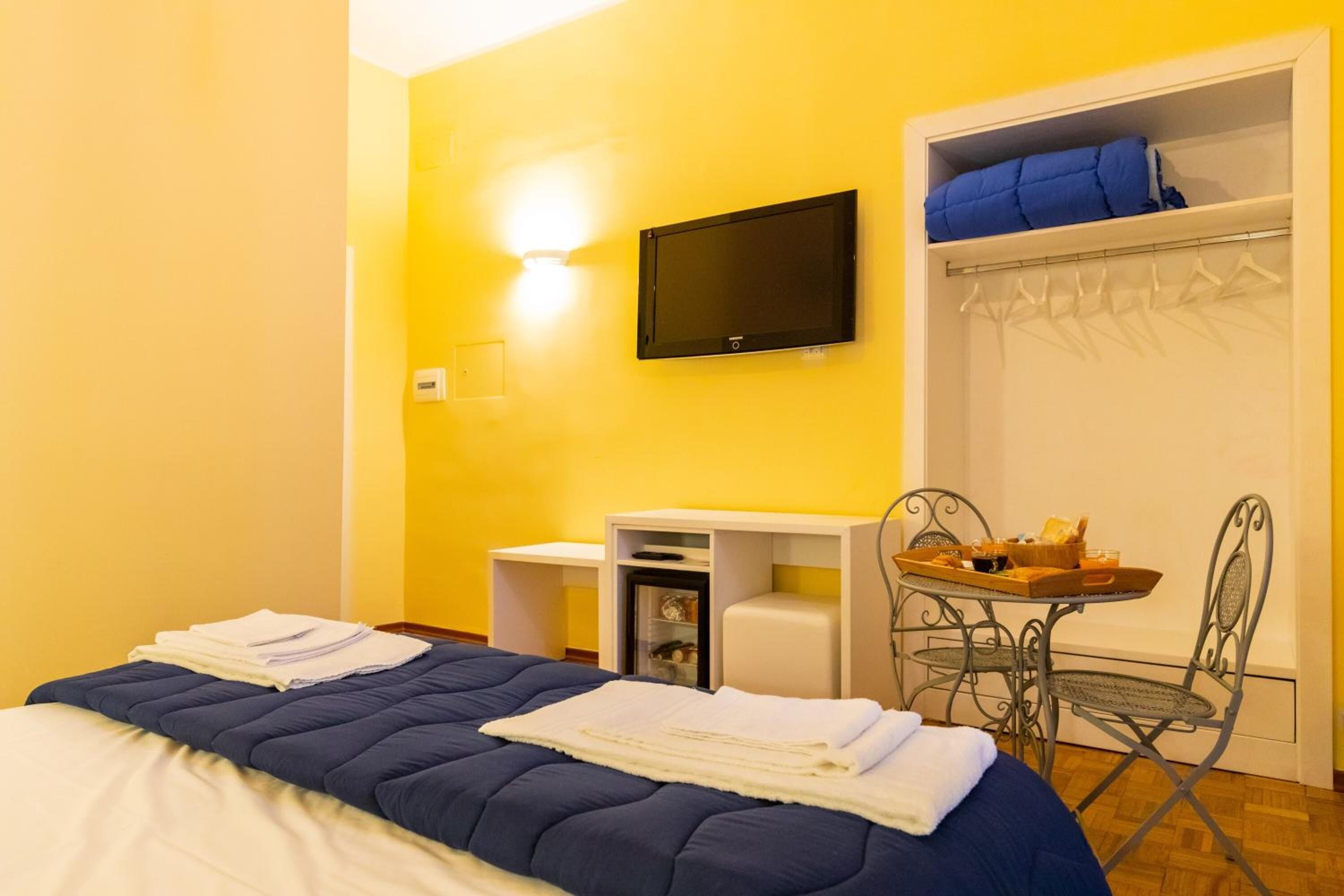 A hotel room with a bed, a desk, a chair, a TV, and a wardrobe.