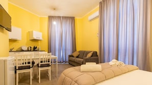 A hotel room with a bed, a sofa, a desk with chairs, and a television. - B&B Trianon (Naples)
