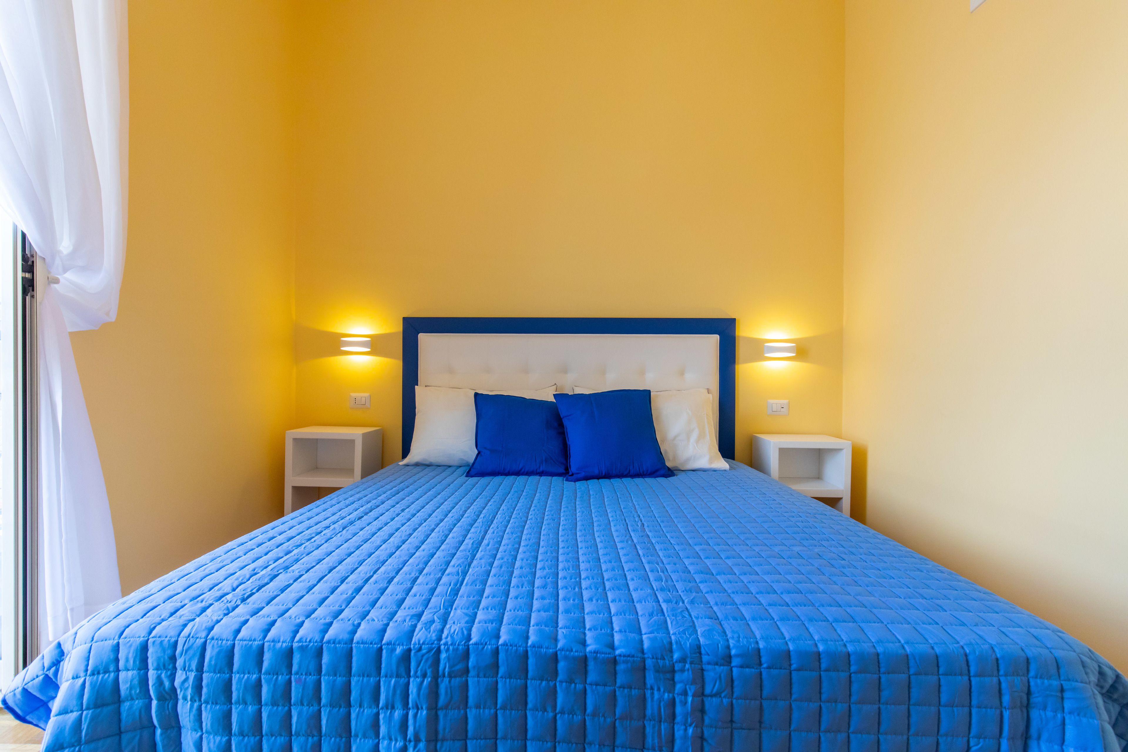 Una cama bien hecha con colcha azul, dos almohadas y un cabecero con luces empotradas.