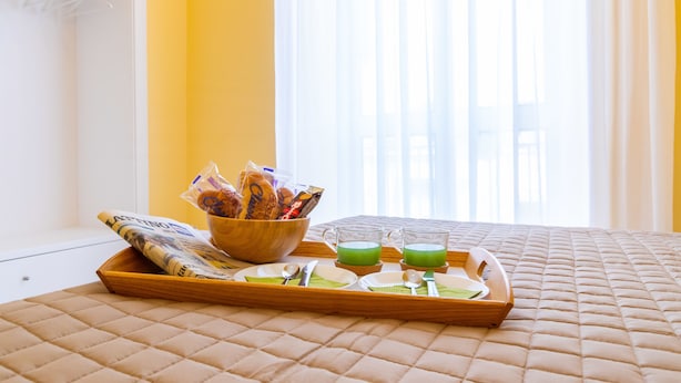A breakfast tray with snacks, green beverages, and a bowl of fruits on a bed with a quilted cover. - B&B Trianon (Naples)