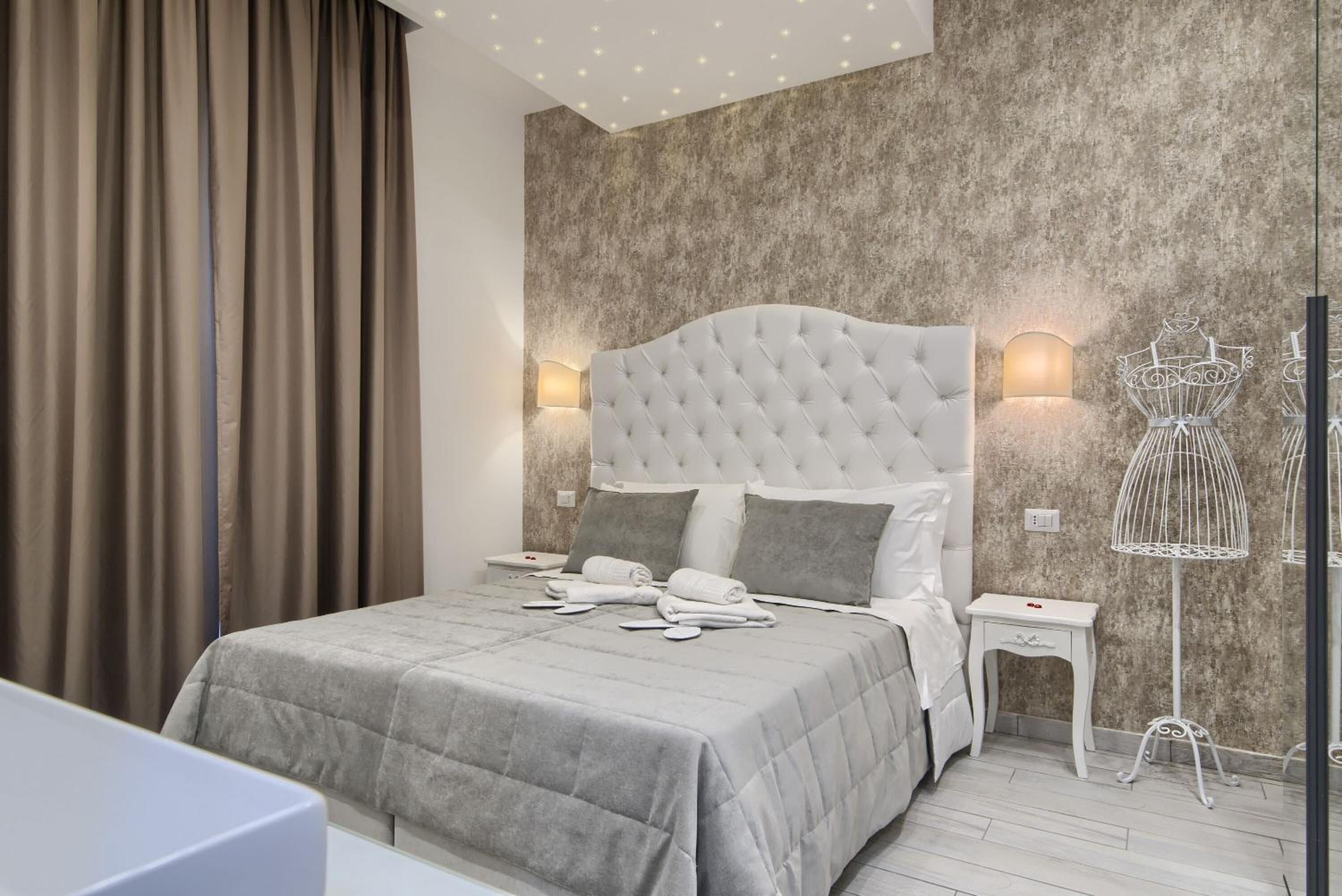 Un dormitorio moderno con cabecera capitonada, colcha acolchada gris, lámparas de noche y una lámpara de pie decorativa.
