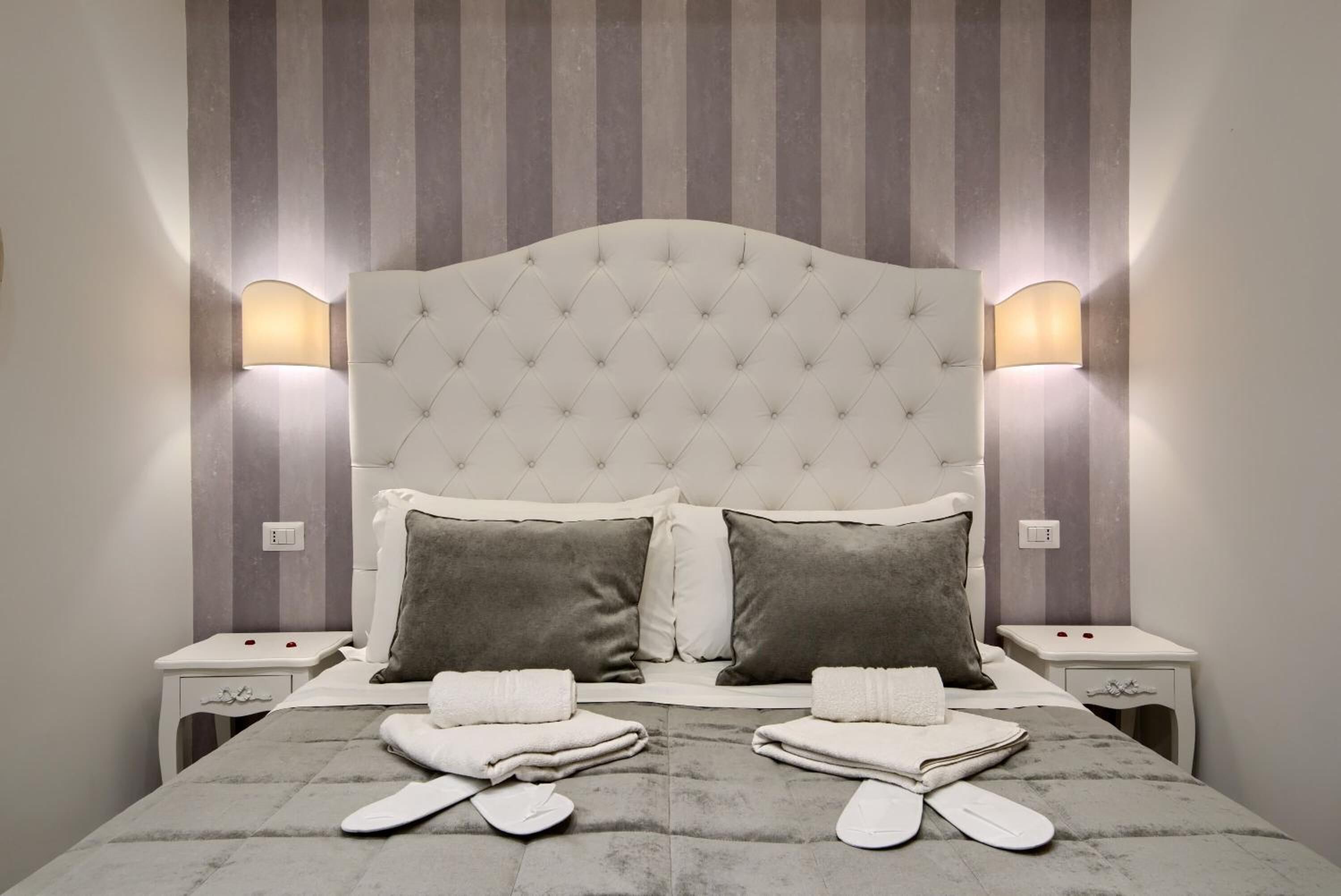 A neatly made bed with a tufted headboard, two bedside tables, and wall-mounted lamps.