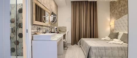 A modern hotel room with a large bed, a built-in vanity with a mirror, a shower area, and a bedside table with a lamp.