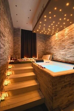 Une salle de spa dotée d’une baignoire en bois, d’un escalier menant à un balcon et d’un mur en pierre.