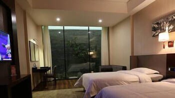A hotel room with two beds, a desk, a chair, a TV, and a large window with a view of trees. - Xinyiyuan Hotel (Changsha)