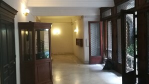 Um corredor amplo com piso de mármore, portas de madeira e luminárias fixadas na parede.