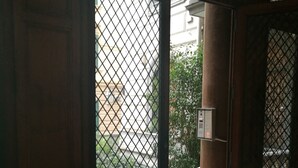 Uma porta de madeira com grade de metal, dando acesso a uma área externa com varanda e um pilar.