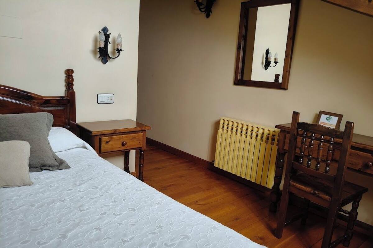 Une chambre à coucher comprenant un lit, une table de chevet, une chaise, un radiateur et un miroir accroché au mur.