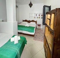 Quarto com duas camas, um guarda-roupa de madeira, televisão e uma estante na parede com objetos decorativos.