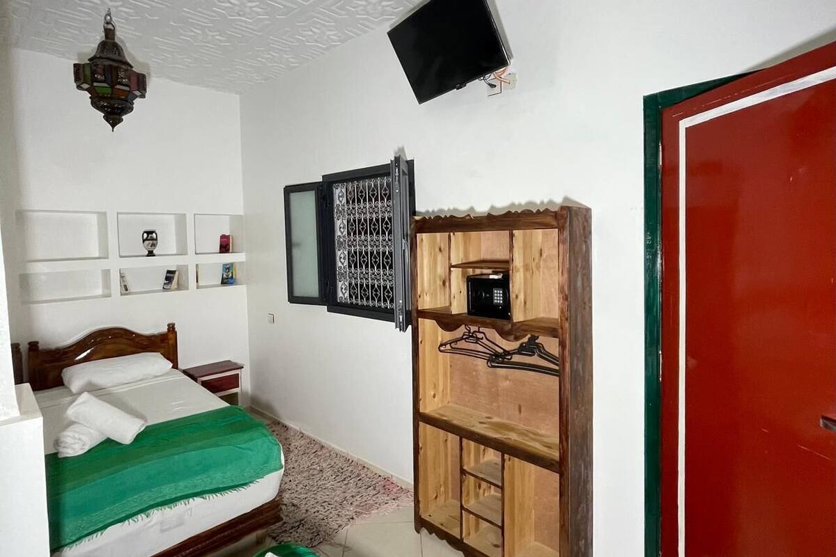 A hotel room with two beds, a wooden wardrobe, a television, and a red door.