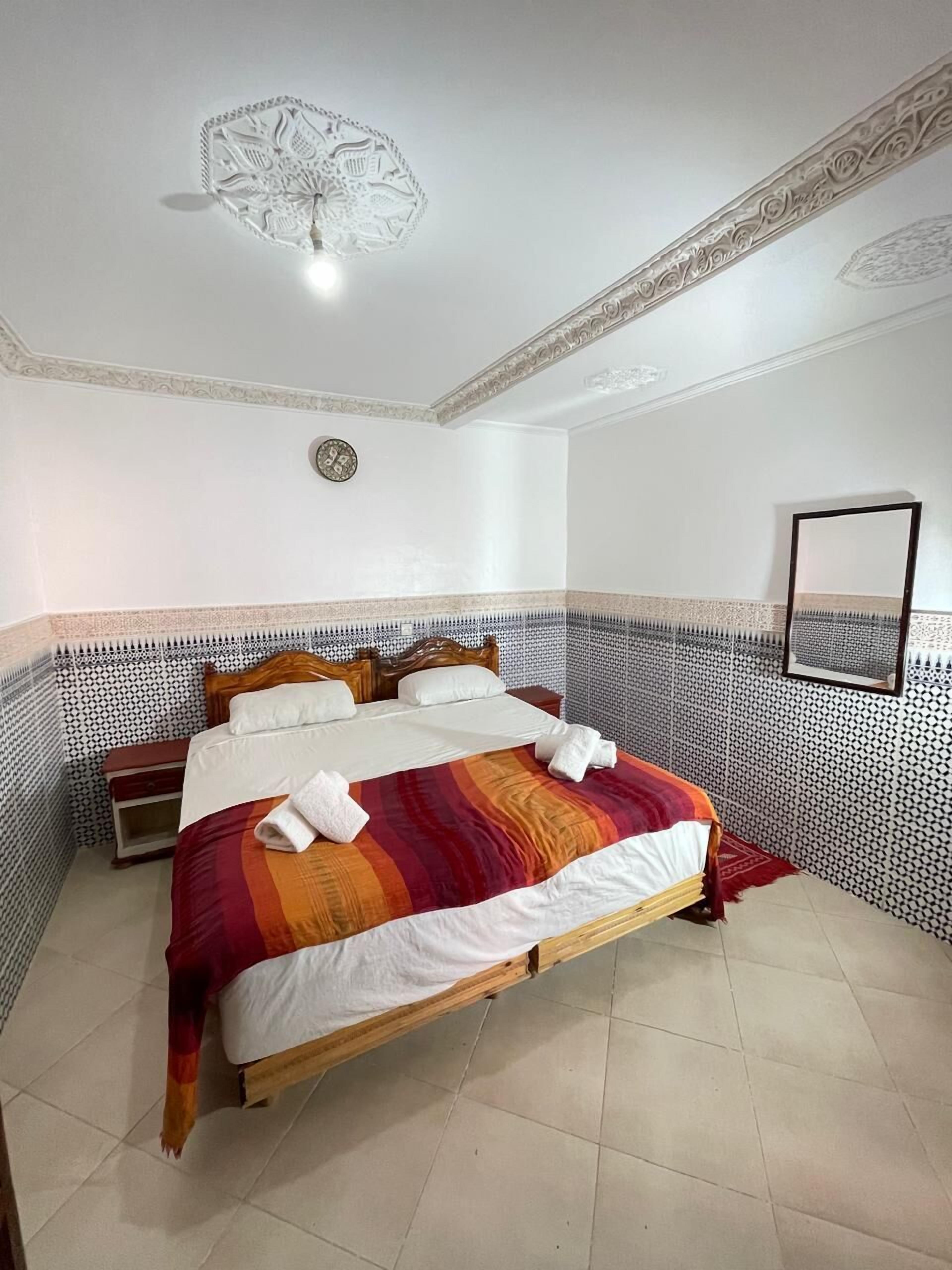 A hotel room with a large bed, a nightstand, a mirror, and a decorative ceiling light.