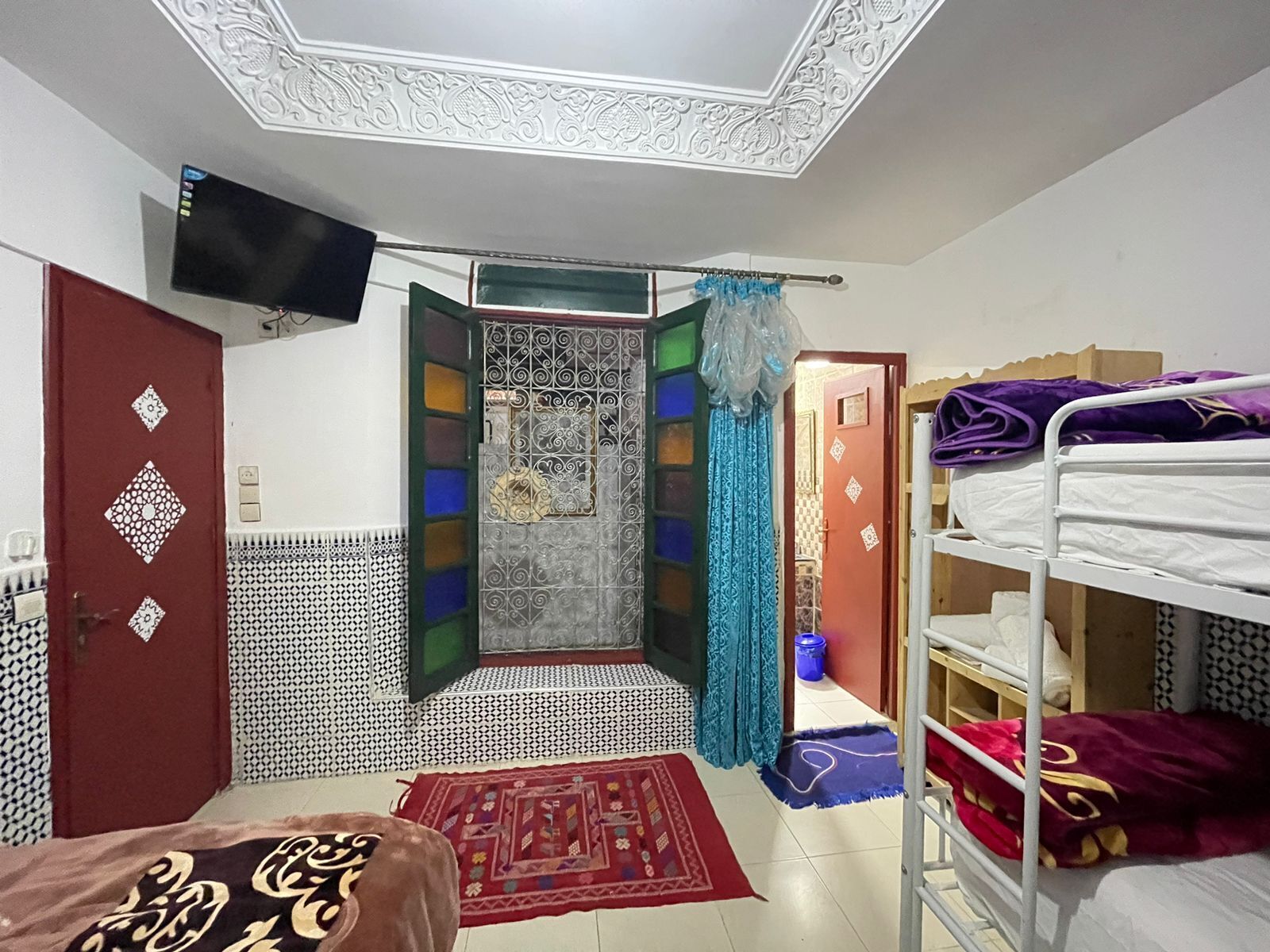 A room with a bed, a TV mounted on the wall, a wardrobe, and a bathroom with a shower curtain.
