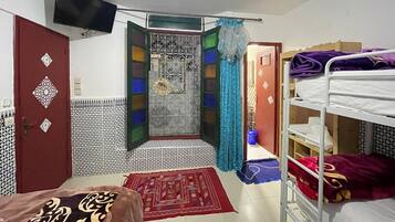 Una habitación con una cama, un televisor montado en la pared, un armario y un baño con cortina de ducha.
