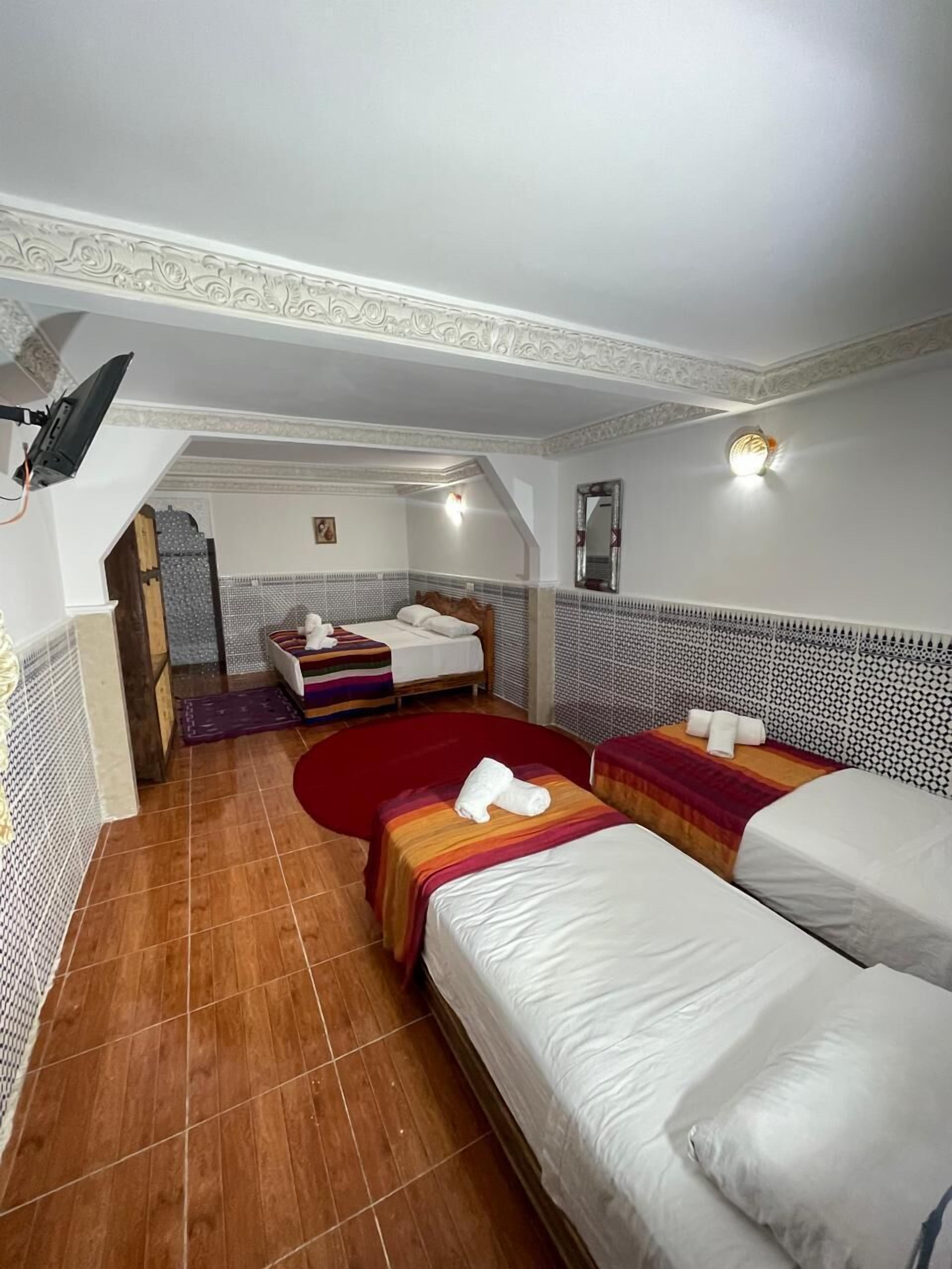 A hotel room with two beds, a small sitting area, and a ceiling fan.