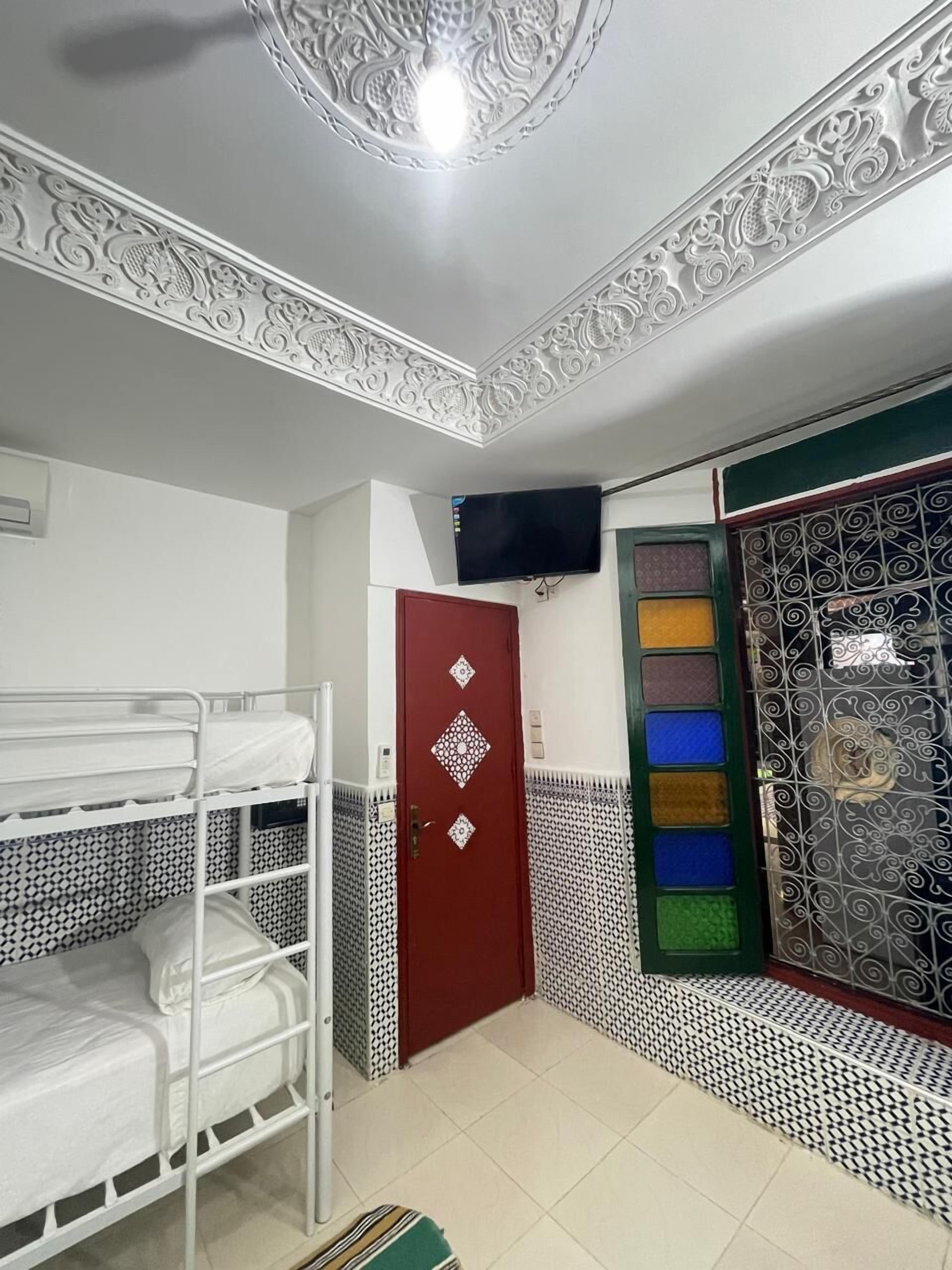 Una habitación con literas, una puerta roja, un televisor montado en la pared y baldosas estampadas en el suelo y las paredes.