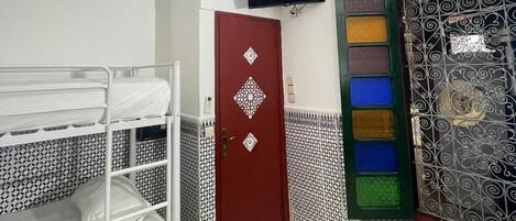 Una habitación con literas, una puerta roja, un televisor montado en la pared y baldosas estampadas en el suelo y las paredes.