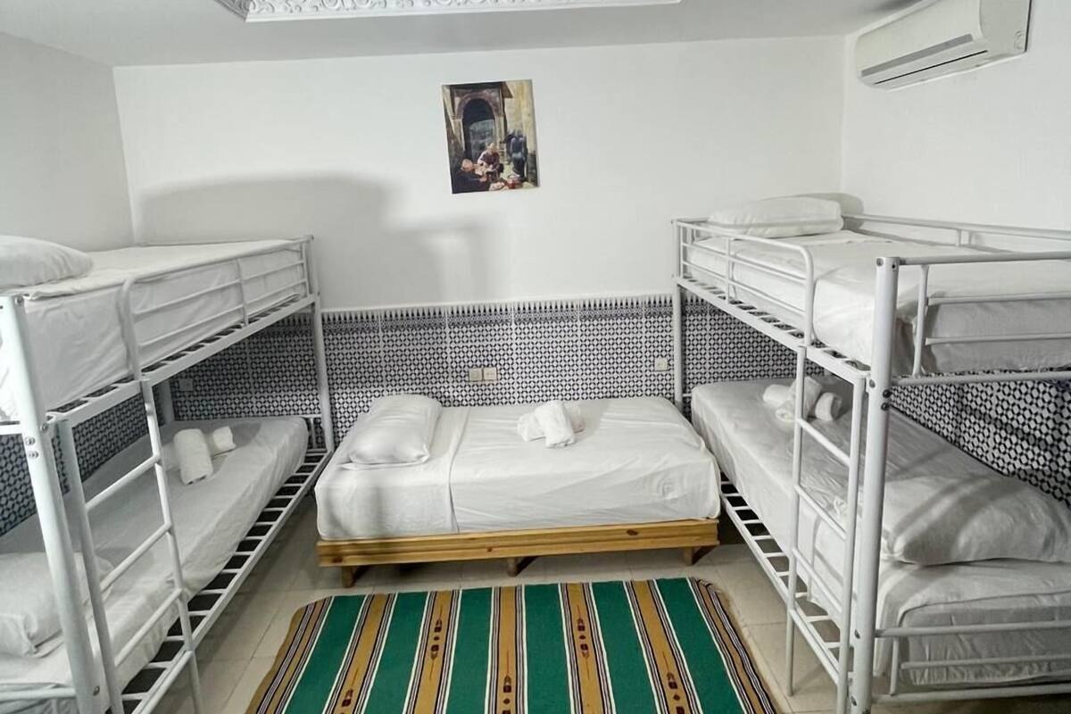 A dormitory room with bunk beds, a patterned rug, a ceiling medallion, and a wall-mounted air conditioner.