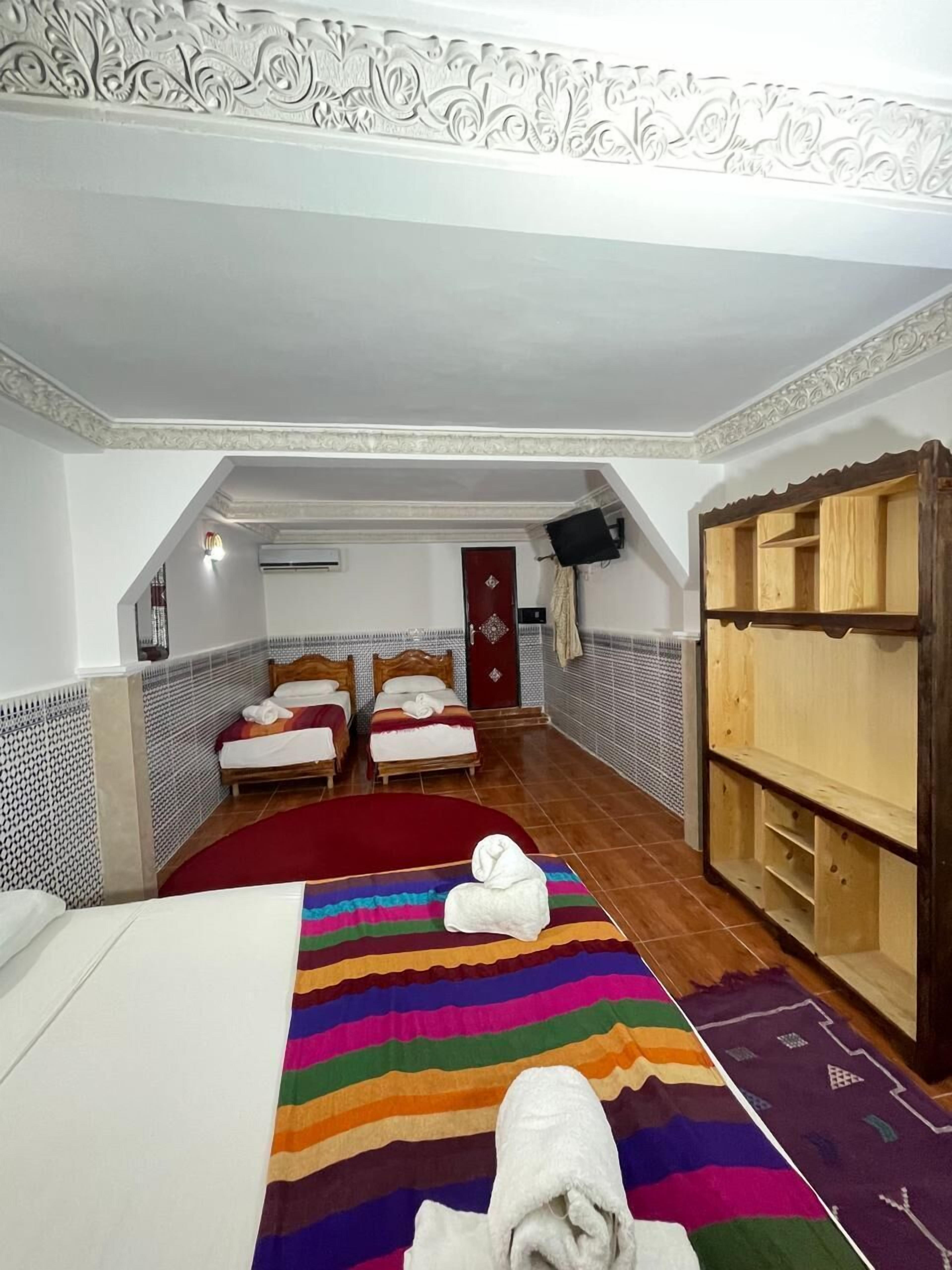 A hotel room with two beds, a red carpet, a wooden wardrobe, and a patterned rug.
