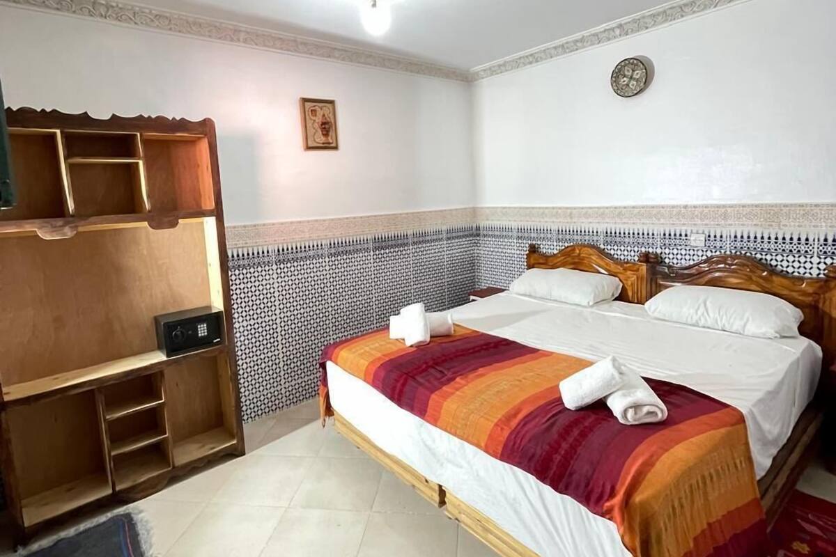 A hotel room with a wooden bed, a built-in wardrobe, a patterned wall, and a ceiling light fixture.