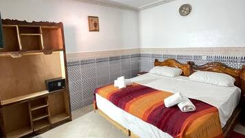 A hotel room with a wooden bed, a built-in wardrobe, a patterned wall, and a ceiling light fixture.