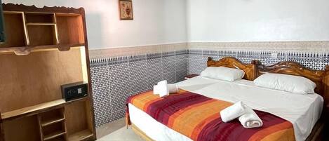 Una habitación de hotel con una cama de madera, un armario empotrado, un papel tapiz decorativo y una lámpara en el techo.