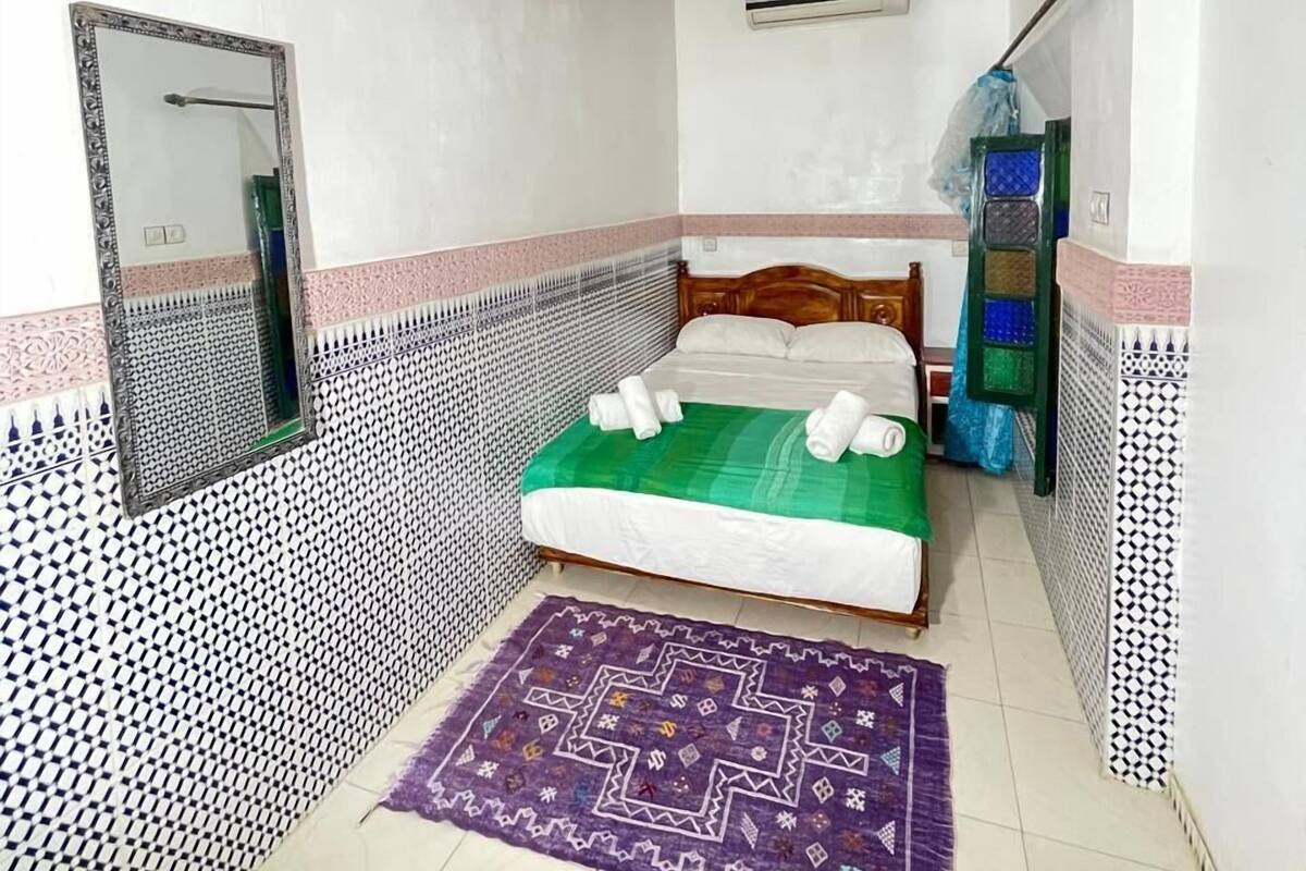 A bedroom with a bed, a mirror, a ceiling fan, and patterned walls.