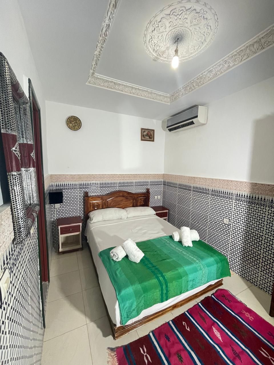 Et soveværelse med en seng, et natbord, en aircondition, dekorativt loft og tapetserede vægge.