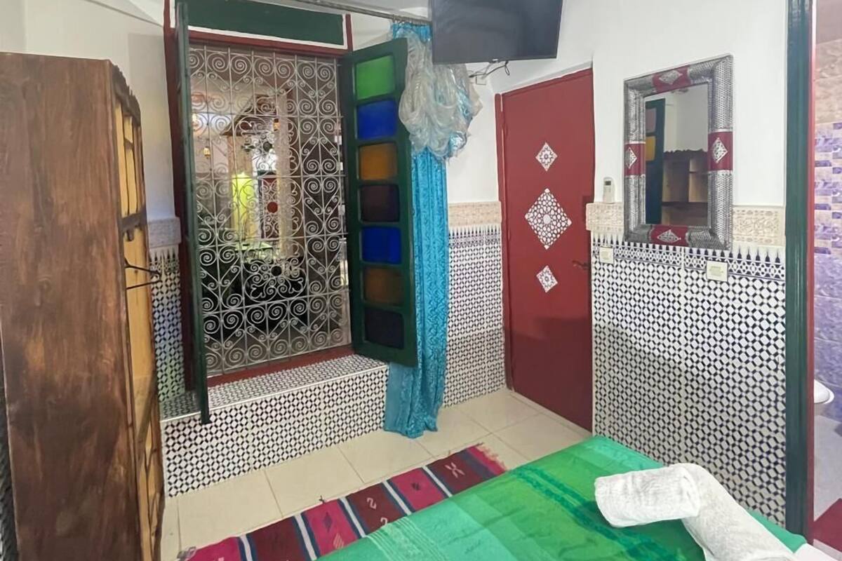A room with a bed, a television, a decorative mirror, and a patterned wall.