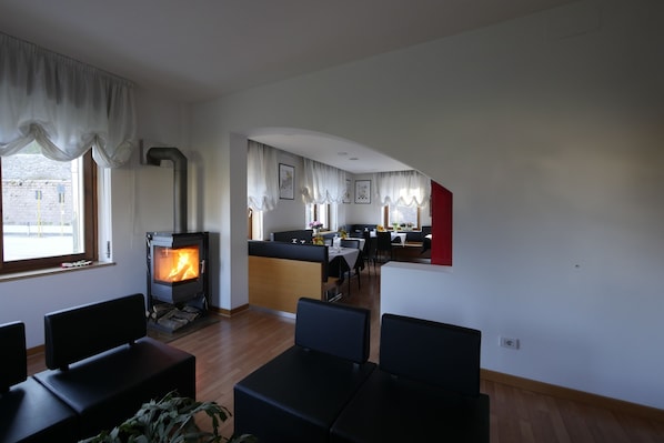 A modern living room with a fireplace, a dining area, and a kitchen with a red accent wall. - Albergo De March (Ponte nelle Alpi)