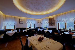 A restaurant with round tables, white tablecloths, and a warm ceiling light. - Albergo De March (Ponte nelle Alpi)