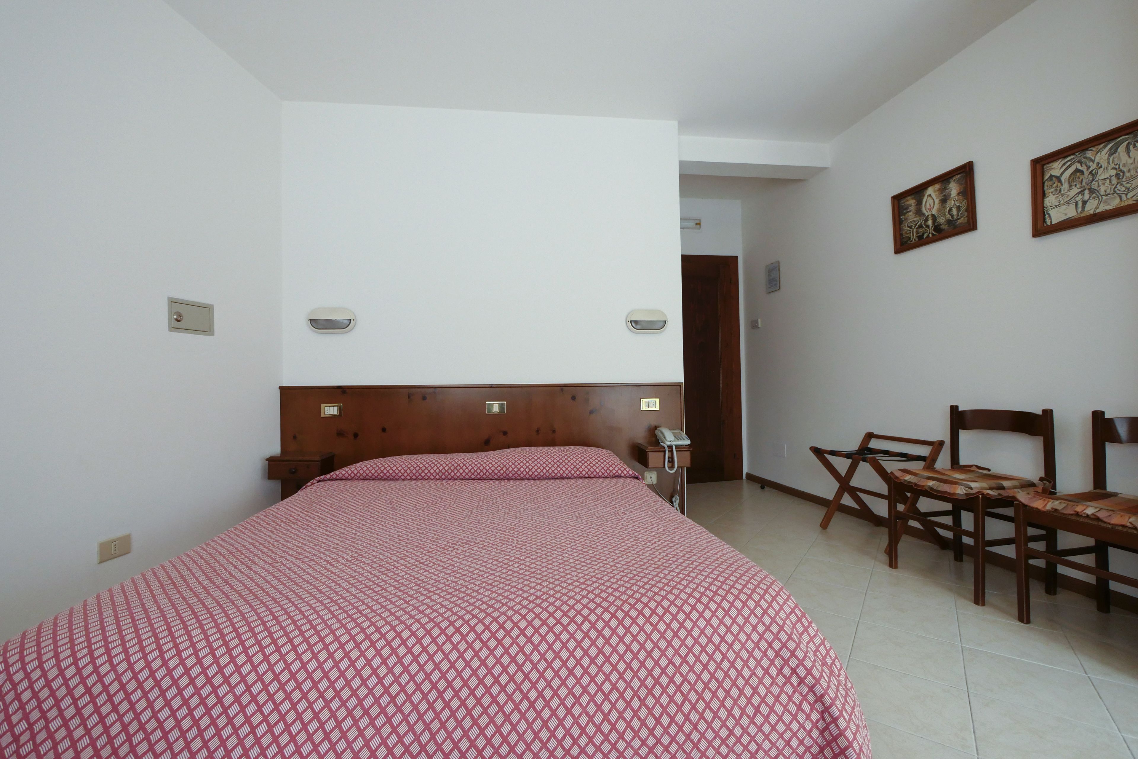 Un dormitorio con cama, cabecera de madera, escritorio con silla y teléfono.