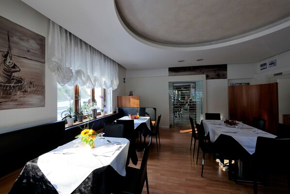 A restaurant with tables set for dining, a large window with curtains, and a painting on the wall. - Albergo De March (Ponte nelle Alpi)