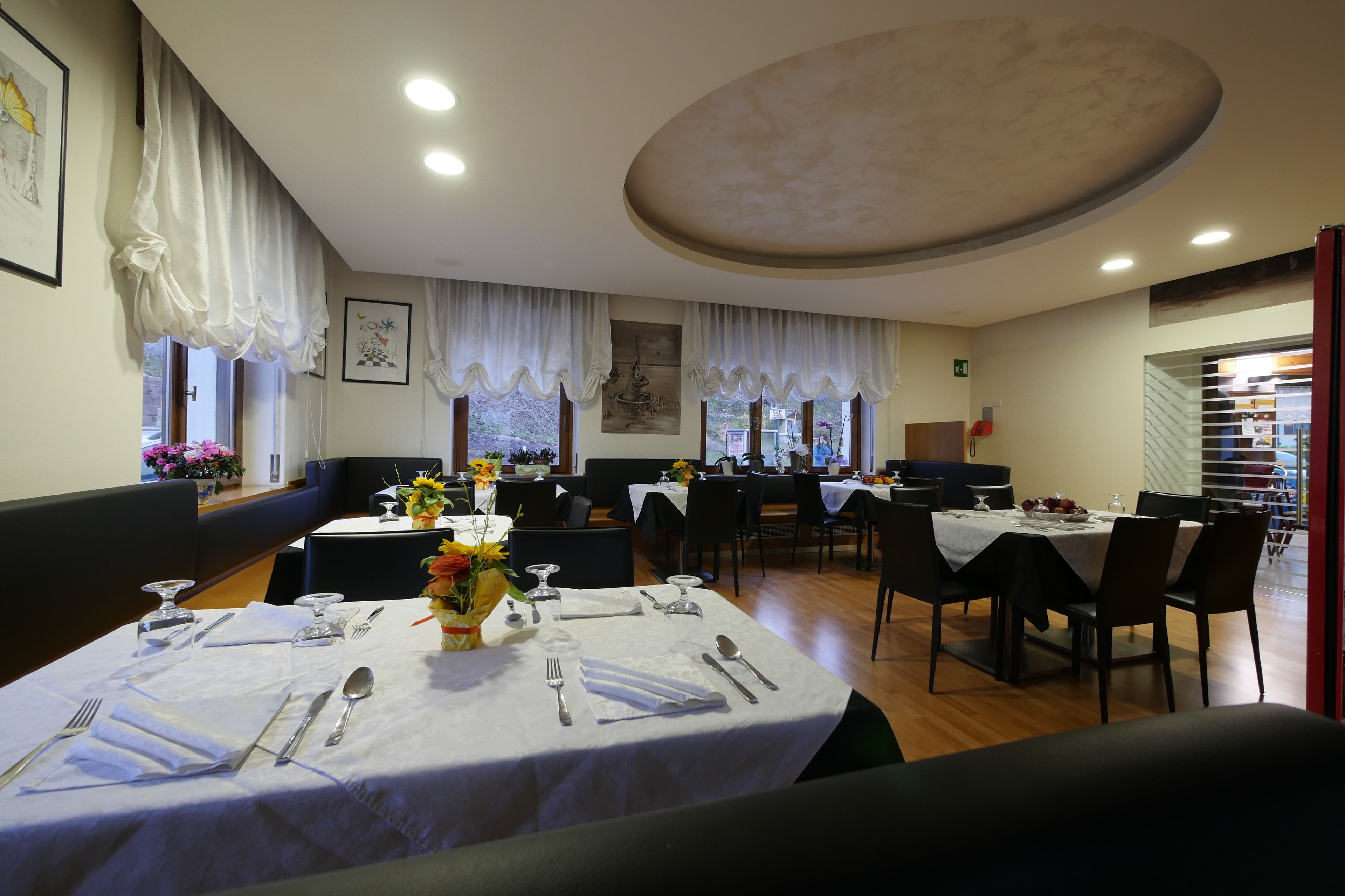 A dining area with tables set for four, each with cutlery and a vase of flowers.