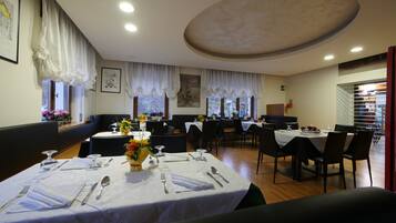 A dining area with tables set for four, each with cutlery and a vase of flowers.
