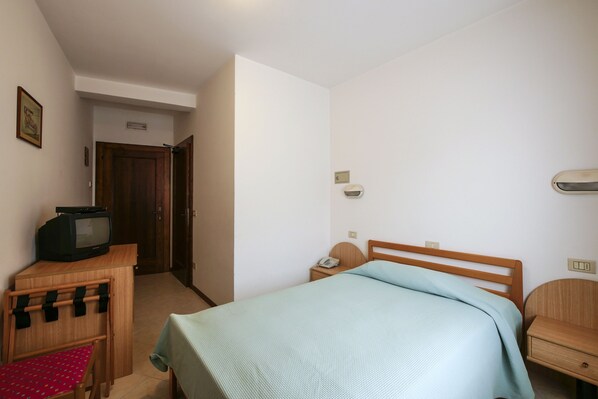 A bedroom with a bed, a wooden nightstand, a small table with a television, and a chair. - Albergo De March (Ponte nelle Alpi)