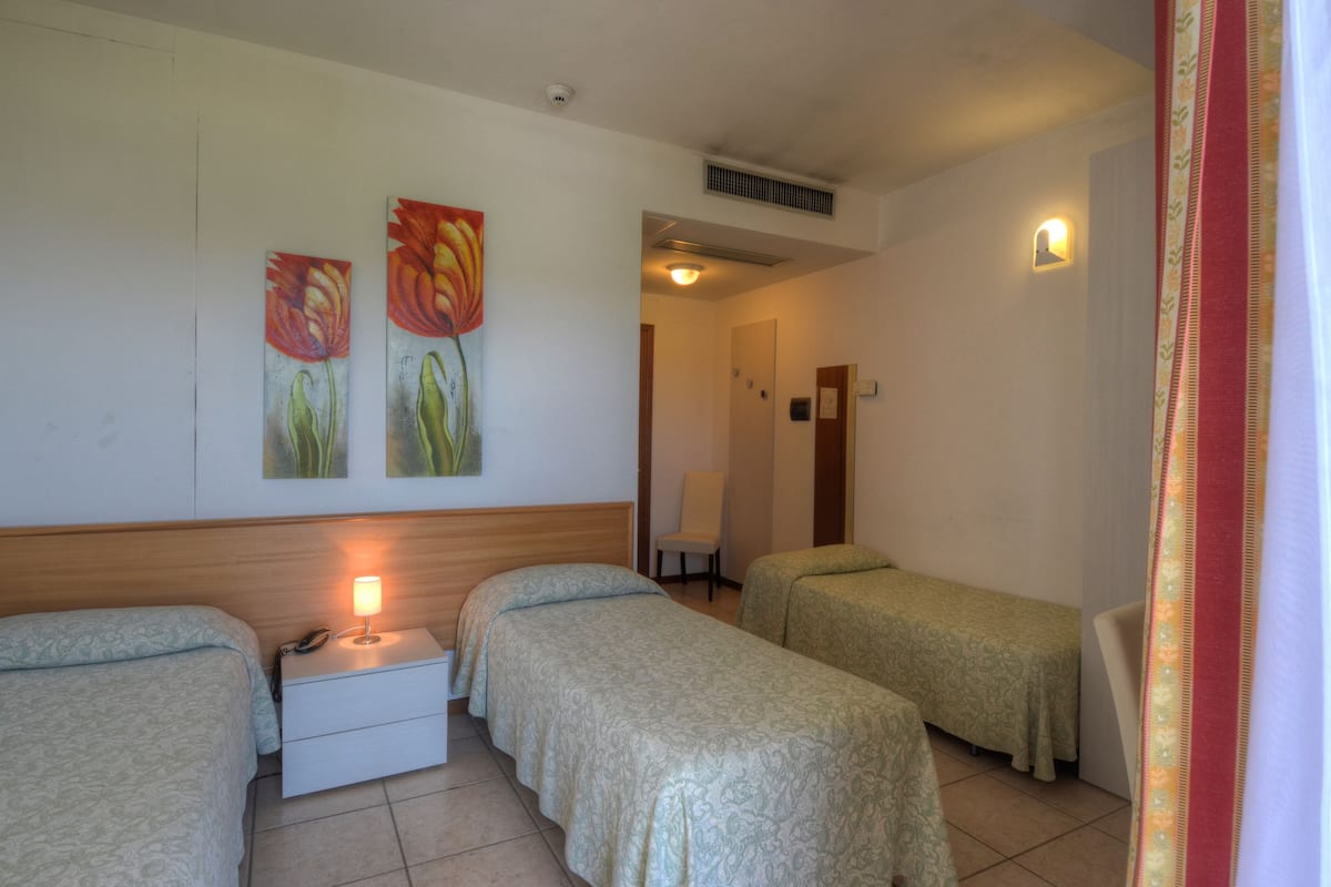 A room with two single beds, a bedside table with a lamp, and a wall-mounted telephone.