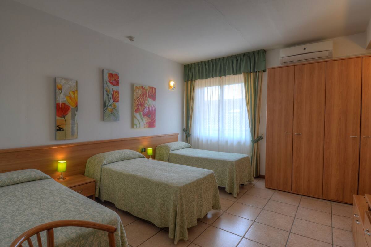 A hotel room with two single beds, a wooden wardrobe, and a nightstand with a lamp.